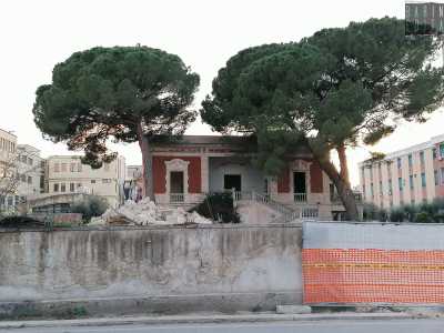 Siamo di fronte al muro perimetrale dell�edificio. Un tempo segnato da un sontuoso ingresso, oggi � chiuso dalla recinzione dei lavori in corso che lasciano comunque intravedere la facciata rossa e bianca della villa...